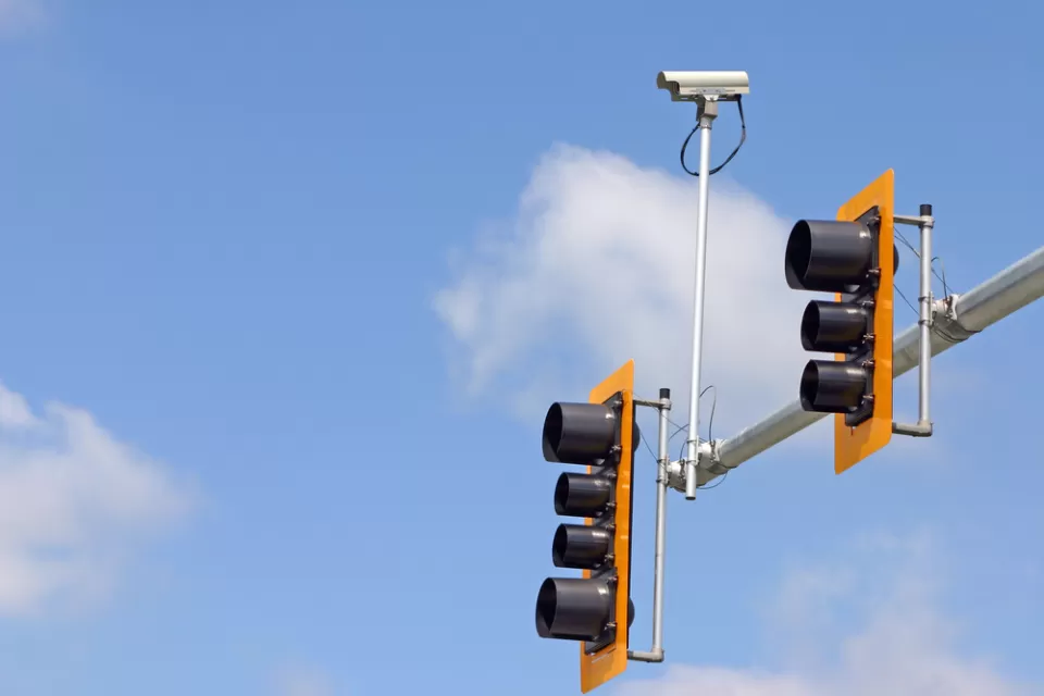 Stoplight with two lights and mounted traffic camera against blue sky with white clouds